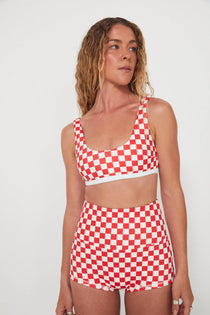 Woman wearing a red and white checkered two-piece, bralette swim top and original betty bottoms outfit on a plain background