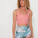 Woman wearing a red and white checkered punchy surf top and patterned ocean photographed shorts on a white background