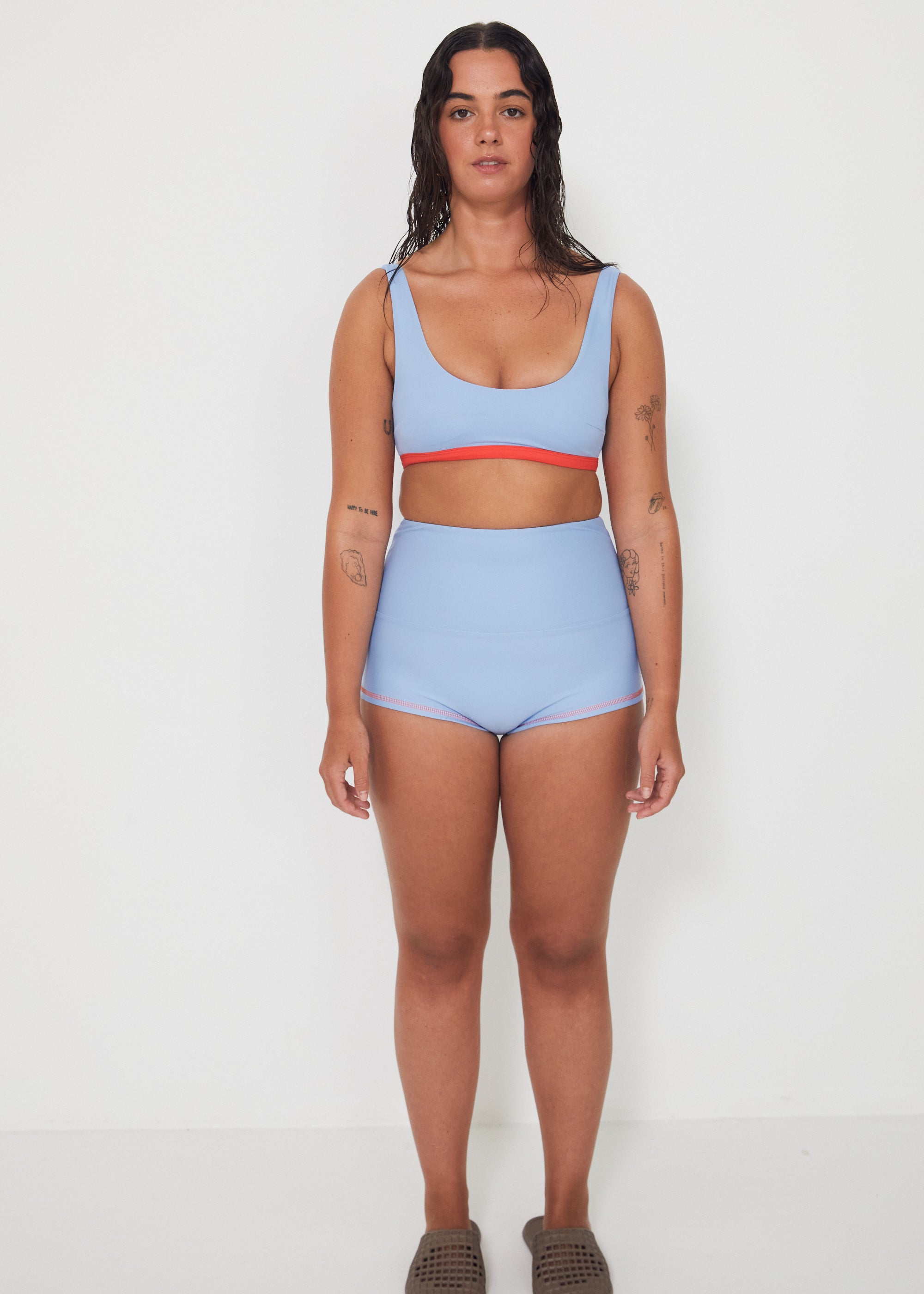 Woman wearing a light blue bralette bikini and original betty bottoms with a white background