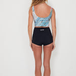 Woman wearing a patterned crop top and black shorts on a white background