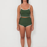 Woman wearing a green tankini surf top and betty bottoms 2.0 swimsuit with white trim against a white background