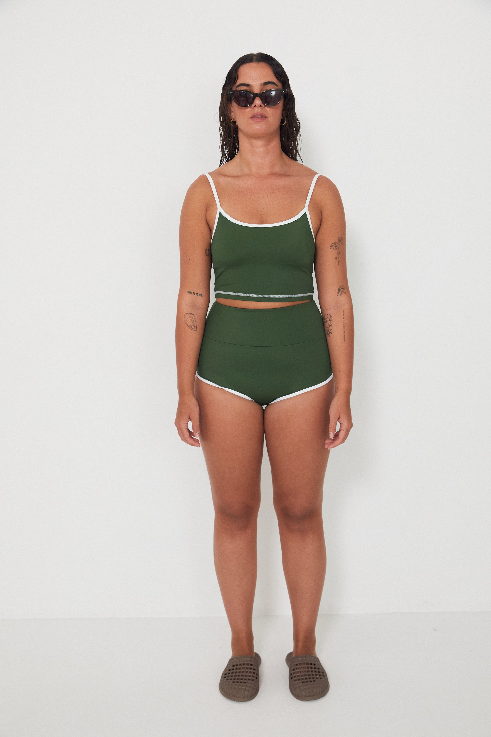 Woman wearing a green tankini surf top and betty bottoms 2.0 swimsuit with white trim against a white background