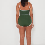 Woman wearing a green tankini surf top and betty bottoms 2.0 swimsuit with white trim against a white background