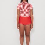 Person wearing a red and white checkered low rider rashugard top and red original betty bottoms shorts on a white background