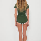 Woman wearing a green olive low rider rashguard and betty bottoms 2.0 with white trim on a plain background