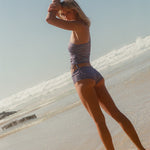 Woman in a striped swimsuit standing on a beach with clear sky