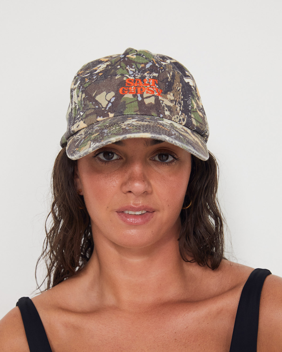 Woman wearing a camouflage dad cap with a red 'Salt Gypsy' logo on a white background